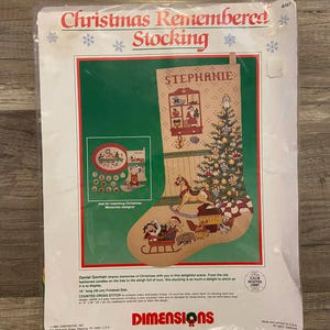 May include: A cross-stitch kit for a Christmas stocking, packaged in plastic. The design includes a Christmas tree, toys, and the name "Stephanie." The text "Christmas Remembered Stocking" is at the top, with the Dimensions logo at the bottom.