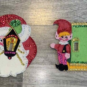 Puede incluir: Cuatro adornos navideños con diseños de Papá Noel y elfo. Los adornos incluyen un Papá Noel con una linterna y un elfo con una puerta verde. Los adornos son rojos, blancos, dorados y verdes.