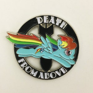 May include: A round, enameled pin featuring a cartoon pony with a rainbow mane and wings, flying through the air. The pin has a black border with the words "DEATH FROM ABOVE" in white lettering. The pony is light blue with a rainbow tail.