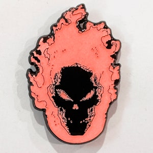Könnte beinhalten: Eine rosa und schwarze Emaille-Anstecknadel mit einem Totenkopf mit Flammen. Der Totenkopf ist schwarz mit weißen Details und die Flammen sind leuchtend pink.