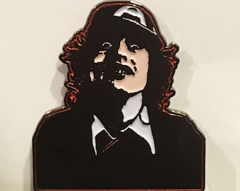 May include: Black and white enamel pin of a person with long curly hair wearing a black hat and a white collared shirt.