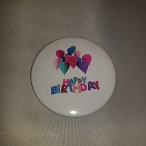 May include: A white button with a colorful happy birthday design featuring balloons and the words "Happy Birthday".