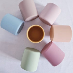 May include: Seven silicone cups in various colours, including light blue, light green, light pink, beige, and brown, arranged in a circle on a white surface.
