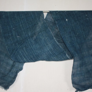 May include: A rectangular piece of indigo-dyed fabric with a visible woven texture. The textile features a deep blue colour with subtle variations in tone and small, light-coloured flecks scattered across the surface, draped over a thin metal rod.