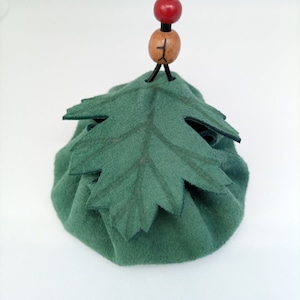 Könnte beinhalten: Ein grüner Filzbeutel mit einem Blattdesign und einer schwarzen Schnur mit Holz- und roten Perlen.