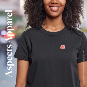 Könnte beinhalten: Schwarzes T-Shirt mit Rundhalsausschnitt und kleinem rotem Briefmarken-Design auf der Brust. Der Text "Aspects Apparel" ist vertikal auf der linken Seite des Bildes aufgedruckt. Designs auf Mockups, Endprodukt kann variieren.