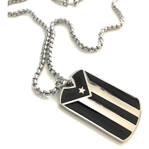 May include: A silver chain necklace with a silver dog tag pendant featuring the Puerto Rican flag. The flag is black and white with a red star in the center.