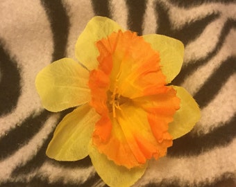 May include: A yellow and orange daffodil flower on a black and white zebra print fabric.
