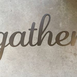 May include: A metal sign with the word "gather" written in a cursive font.