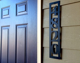 May include: Black metal house number plaque with the numbers 4820 displayed vertically. The plaque is mounted on a light brown wooden wall.