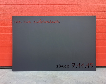 May include: A dark gray metal sign with the text "on an adventure since 7.11.15" in black lettering.