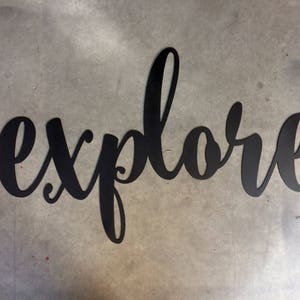 May include: Black metal wall decor with the word "explore" written in a cursive font.