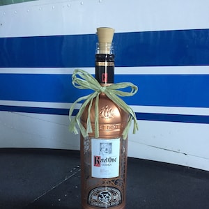 May include: A copper-colored bottle of Ketel One Vodka with a green ribbon and a cork stopper. The bottle is a commemorative bottle celebrating 325 years of the Solent Distillery.