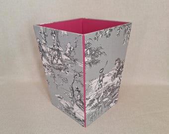 May include: A gray and white decorative wastebasket with a pink interior. The exterior features a toile design with figures and landscapes. The wastebasket has a trapezoidal shape.