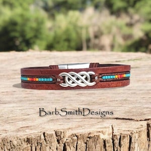 May include: A white ceramic mug with a black handle and the text "But First, Coffee" in a bold, black font. The mug is set against a blurred background, suggesting a cozy setting.