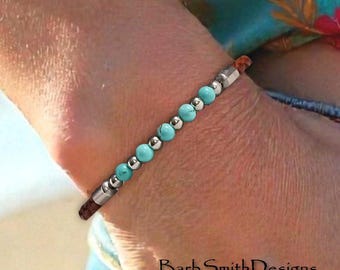 May include: A beaded bracelet featuring alternating turquoise-colored round beads and small metallic silver-toned spherical beads, finished with brown cord ends and silver-toned cylindrical accents. The text BarbSmithDesigns is visible.