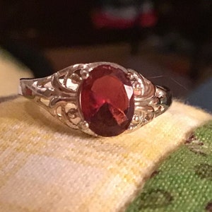 May include: A silver ring with an oval-shaped red gemstone set in a filigree design.