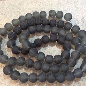 Könnte beinhalten: Eine Schnur grauer, matter Perlen, die auf einer dünnen Schnur aufgefädelt sind. Die Perlen sind rund und glatt und alle gleich groß.