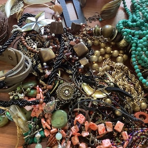 May include: A collection of various necklaces, bracelets, and earrings in a variety of colors and materials. The jewelry includes beaded necklaces, leather bracelets, and gold-toned chains. There are also pieces with turquoise and coral accents.