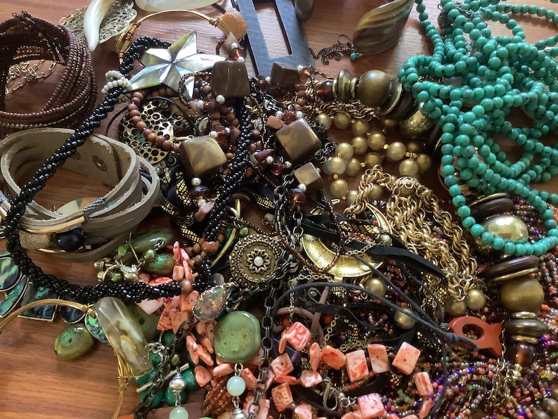 May include: A collection of various necklaces, bracelets, and earrings in a variety of colors and materials. The jewelry includes beaded necklaces, leather bracelets, and gold-toned chains. There are also pieces with turquoise and coral accents.