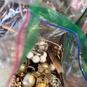 Puede incluir: Una bolsa de pl&aacute;stico llena de una variedad de joyas vintage, incluyendo collares de perlas, broches de oro y pendientes de plata.
