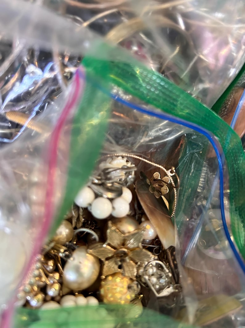 Puede incluir: Una bolsa de pl&aacute;stico llena de una variedad de joyas vintage, incluyendo collares de perlas, broches de oro y pendientes de plata.