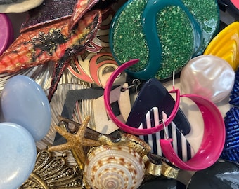 May include: A collection of colorful and unique earrings, including a pair of large green glitter earrings, a pair of pink and black striped earrings, and a pair of black and white striped earrings. There are also several other earrings, including a pair of blue and white earrings, a pair of gold earrings, and a pair of white pearl earrings.
