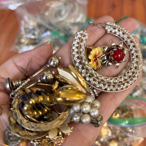 Puede incluir: Una gran colecci&oacute;n de pendientes vintage, incluyendo un par de pendientes grandes de aro con pedrer&iacute;a y un dise&ntilde;o de flor roja y amarilla.
