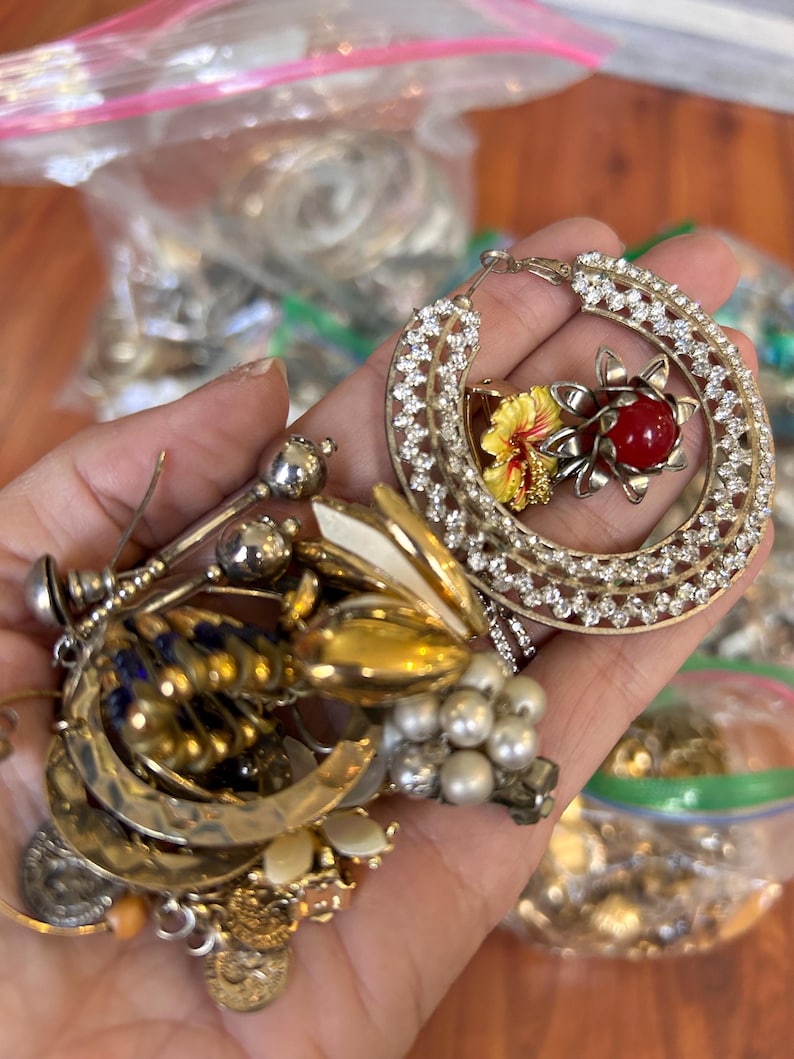 Puede incluir: Una gran colecci&oacute;n de pendientes vintage, incluyendo un par de pendientes grandes de aro con pedrer&iacute;a y un dise&ntilde;o de flor roja y amarilla.