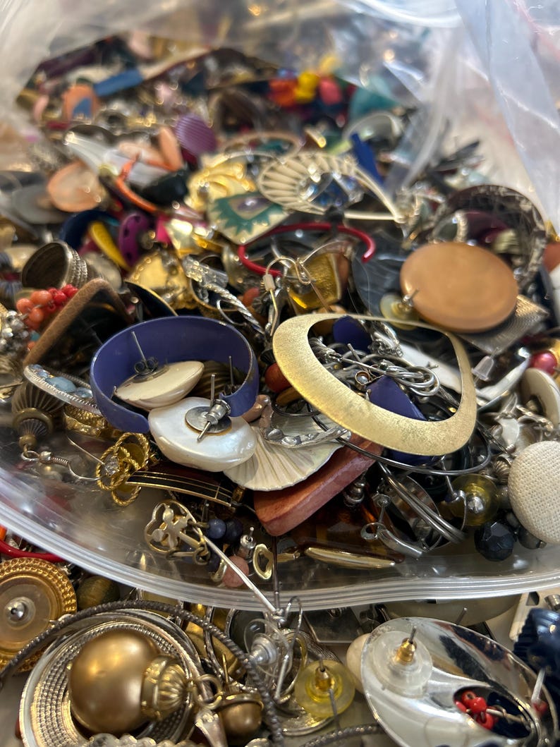 Puede incluir: Una gran bolsa de pl&aacute;stico llena de una variedad de pendientes vintage. Los pendientes est&aacute;n hechos de diferentes materiales, incluyendo metal, pl&aacute;stico, madera y vidrio. Vienen en una variedad de colores, incluyendo oro, plata, rojo, azul, verde y marr&oacute;n.