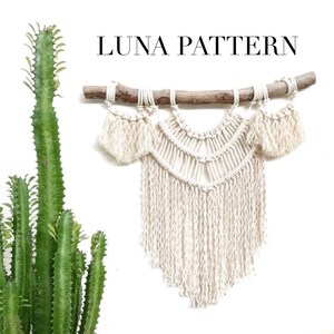 May include: A white macrame wall hanging with a branch at the top and a fringe at the bottom. The macrame is in a crescent shape with a geometric pattern. The text "LUNA PATTERN" is at the top of the image.