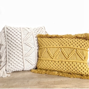May include: Two decorative throw pillows with a macrame design. The pillow on the left is white and the pillow on the right is mustard yellow.