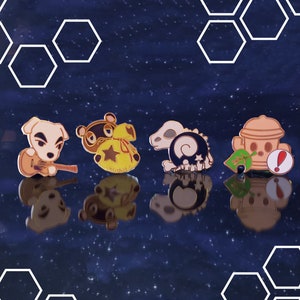 以下が含まれることがあります： アニマル・クロッシングのビデオゲームシリーズのキャラクターをフィーチャーしたエナメルピン4個。ピンはハニカム模様の青い背景の上にあります。ピンは犬、アライグマ、恐竜、消火栓です。