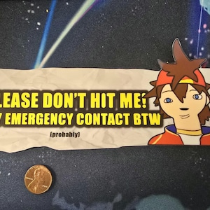 May include: A sticker with the text "PLEASE DON'T HIT ME! MY EMERGENCY CONTACT BTW (probably)" in yellow on a white background. A cartoon character with brown hair and a red hat is on the right. A penny is in the lower left.