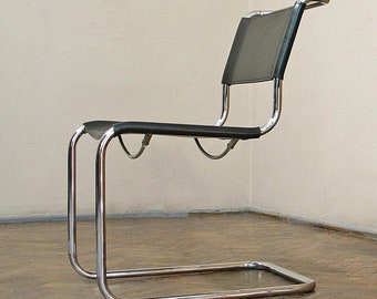 Op de afbeelding: Twee zwarte lederen en chromen cantilever stoelen met een houten vloer op de achtergrond.