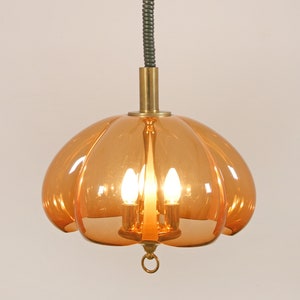 May include: A mid-century modern amber glass pendant light fixture with a brass stem and a black cord. The light fixture has a rounded, pumpkin-shaped design with four bulbs.