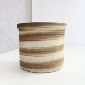 Op de afbeelding: Een witte keramische plantenpot met bruine strepen. De pot is rond en heeft een gladde afwerking.