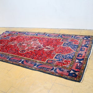 May include: A red and blue rug with a traditional Persian design. The rug has a central medallion and a border with intricate floral and geometric patterns.