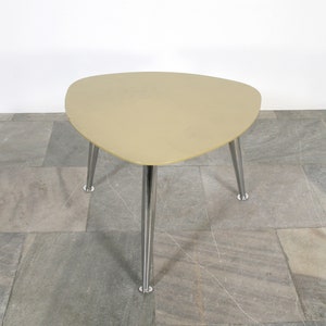 May include: A light beige triangular coffee table with a chrome metal base and three legs.
