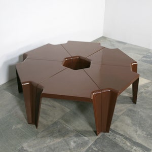 Puede incluir: Una mesa hexagonal de color marrón hecha de cinco piezas separadas que encajan entre sí. La mesa tiene un diseño único con un agujero central en el medio.