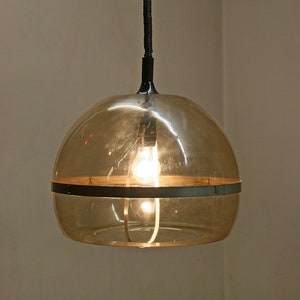 May include: A mid-century modern pendant light with a clear glass shade and a black metal frame. The light is hanging from a black cord and has a light bulb inside.