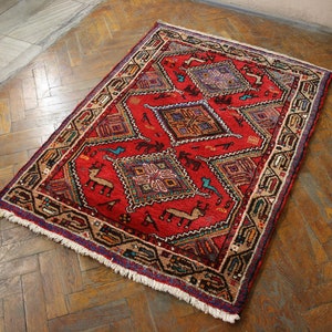 May include: A red, blue, and cream colored rug with a geometric pattern and fringe. The rug has a traditional design with intricate details.