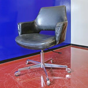 May include: A black leather office chair with a chrome base and five wheels. The chair is in front of a blue and white wall.