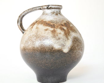 May include: A brown and white ceramic vase with a rounded body and a handle. The vase has a mottled glaze with brown and white streaks.