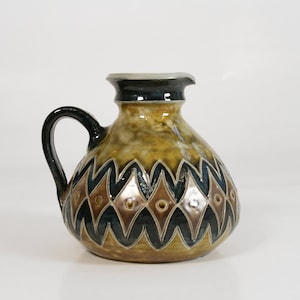 May include: A brown ceramic jug with a black and white geometric pattern. The jug has a rounded body and a handle.