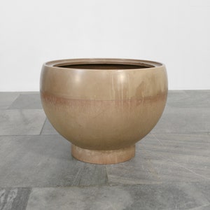 May include: A large, round, brown planter with a wide base. The planter is made of a smooth, textured material.