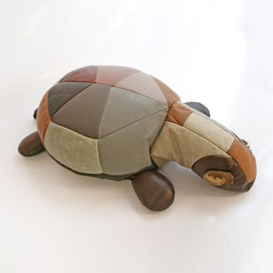 Puede incluir: Un otomano con forma de tortuga de cuero patchwork en tonos marrones, grises y beige.