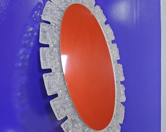 May include: A large oval mirror with a unique, textured, clear glass frame. The frame is made of many small, irregular pieces of glass that create a jagged, almost ice-like effect. The mirror has a red backing.