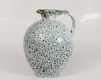 May include: A speckled ceramic pitcher with a rounded body and a handle. The pitcher is glazed in a light blue color with black speckles.