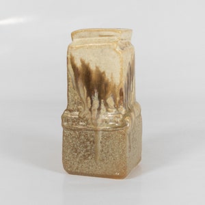 May include: A square ceramic vase with a brown and beige glaze. The vase has a textured surface and a slightly flared opening.